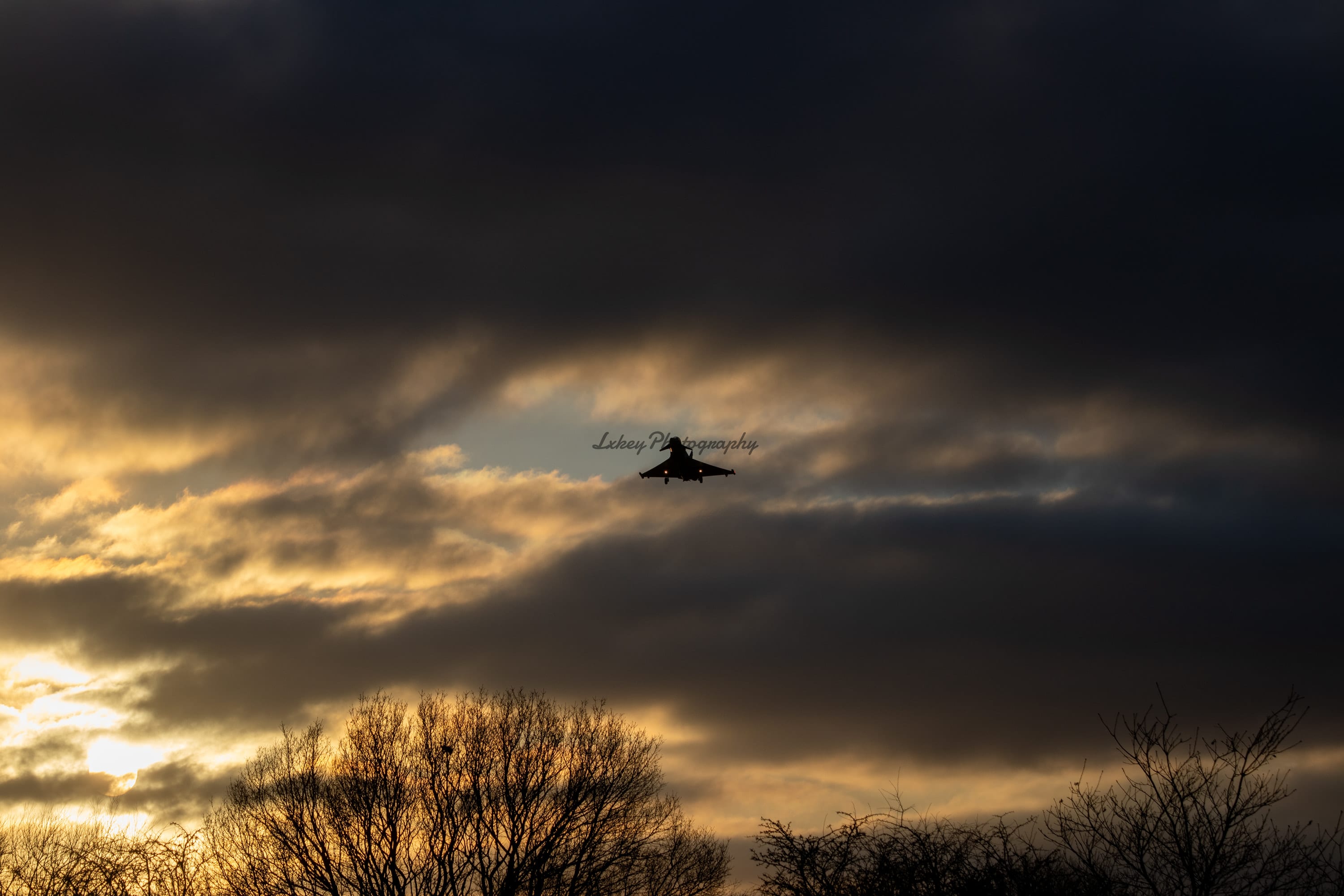 Royal Air Force Typhoon silhouetted on approach beneath a break of gold evening cloud